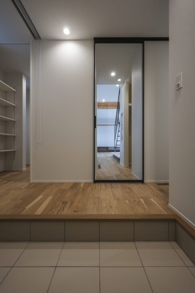 黒枠の室内ドア越しに階段が見える玄関空間