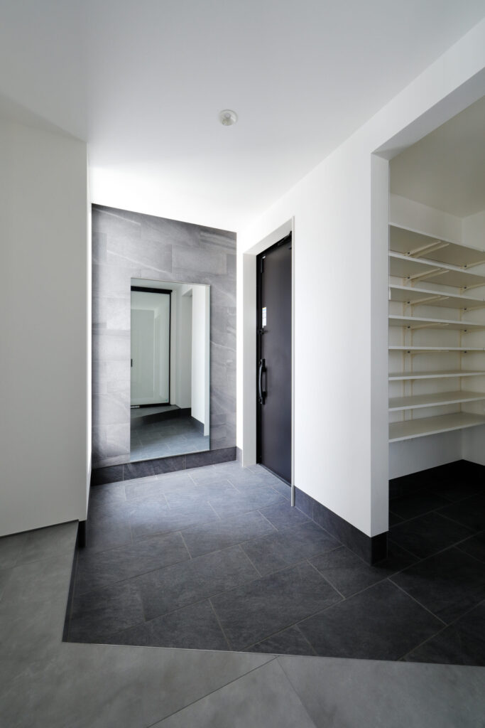 グレーのタイルと大きなミラーが印象的なモダンな玄関